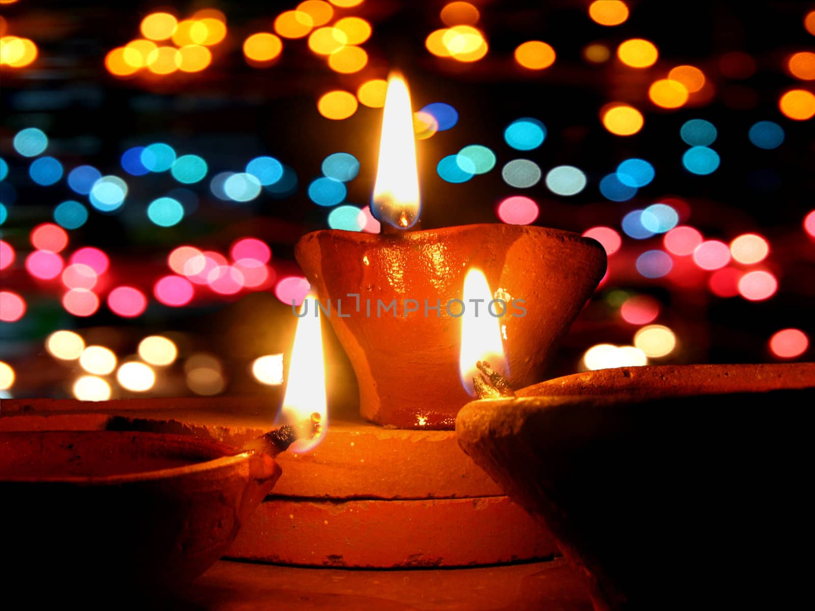 Traditional lamps lit in front of colorful lighting, during Diwali festival in India.
