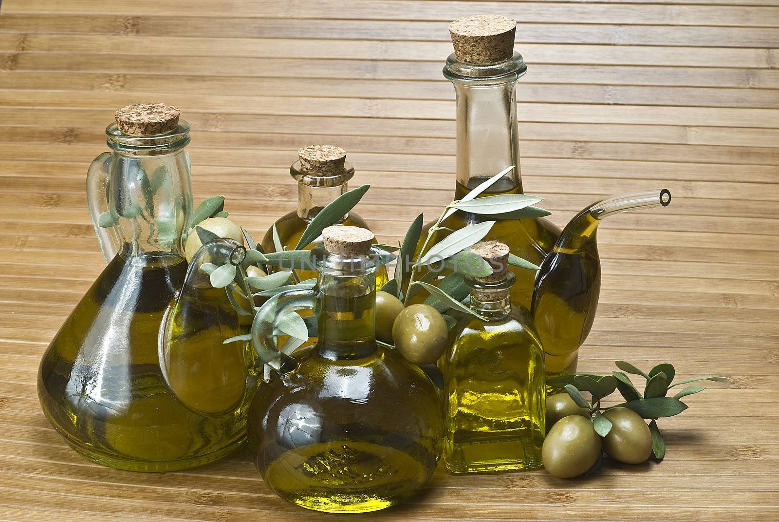 Olive oil bottles and olives on a bamboo mat.