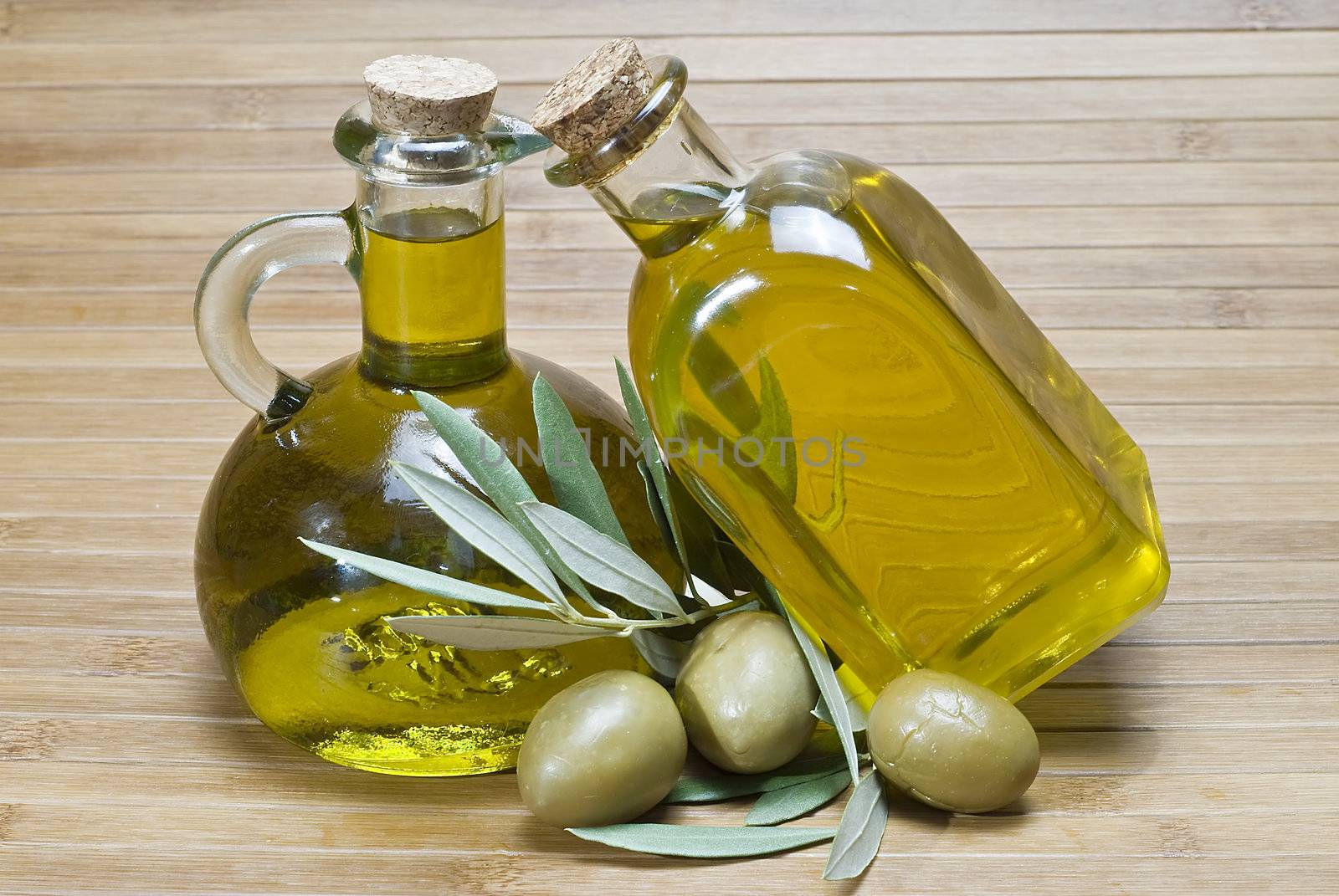 Olive oil bottles and olives on a bamboo mat.