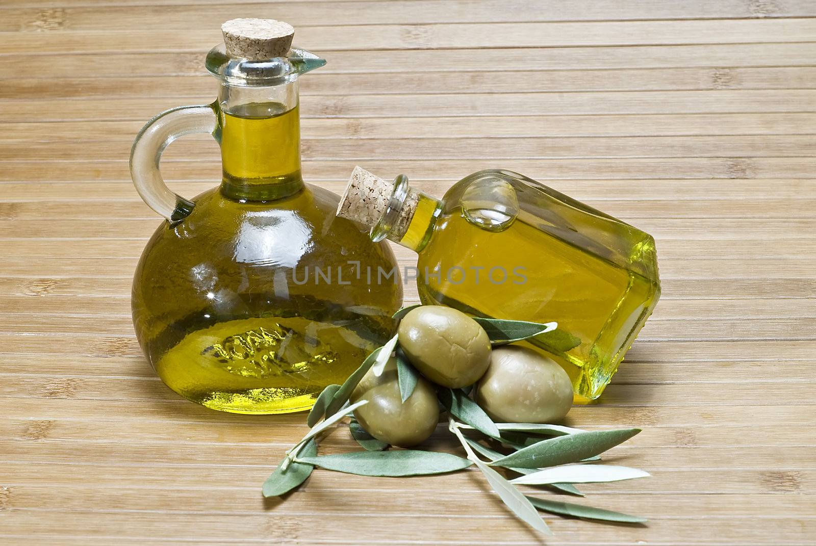 Olive oil bottles and olives on a bamboo mat.