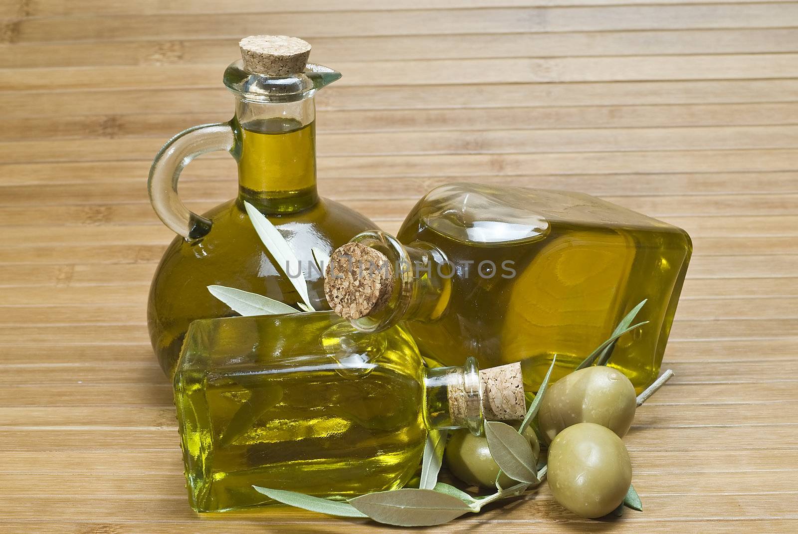 Olive oil bottles and olives on a bamboo mat.