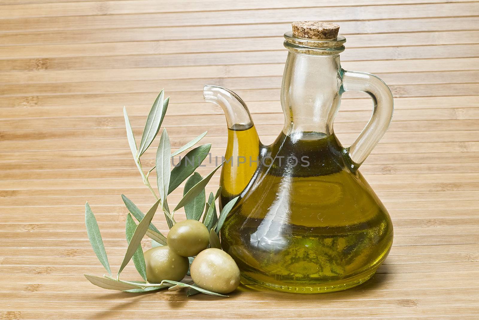 Olive oil bottles and olives on a bamboo mat.