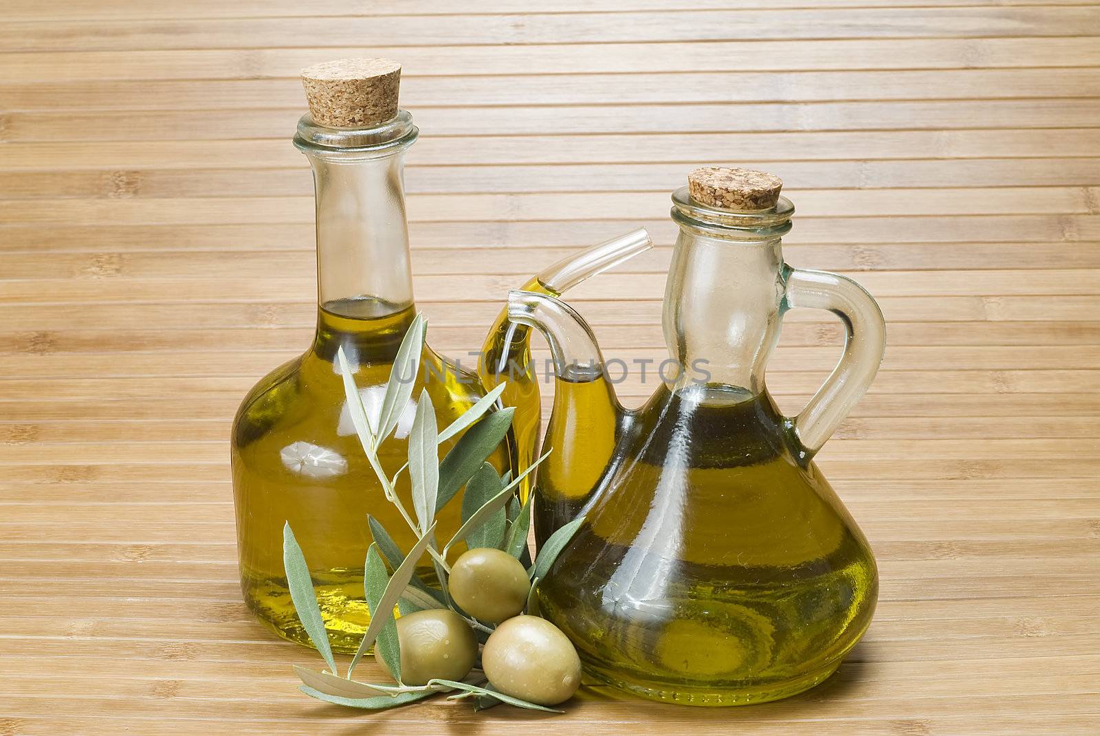 Olive oil bottles and olives on a bamboo mat.