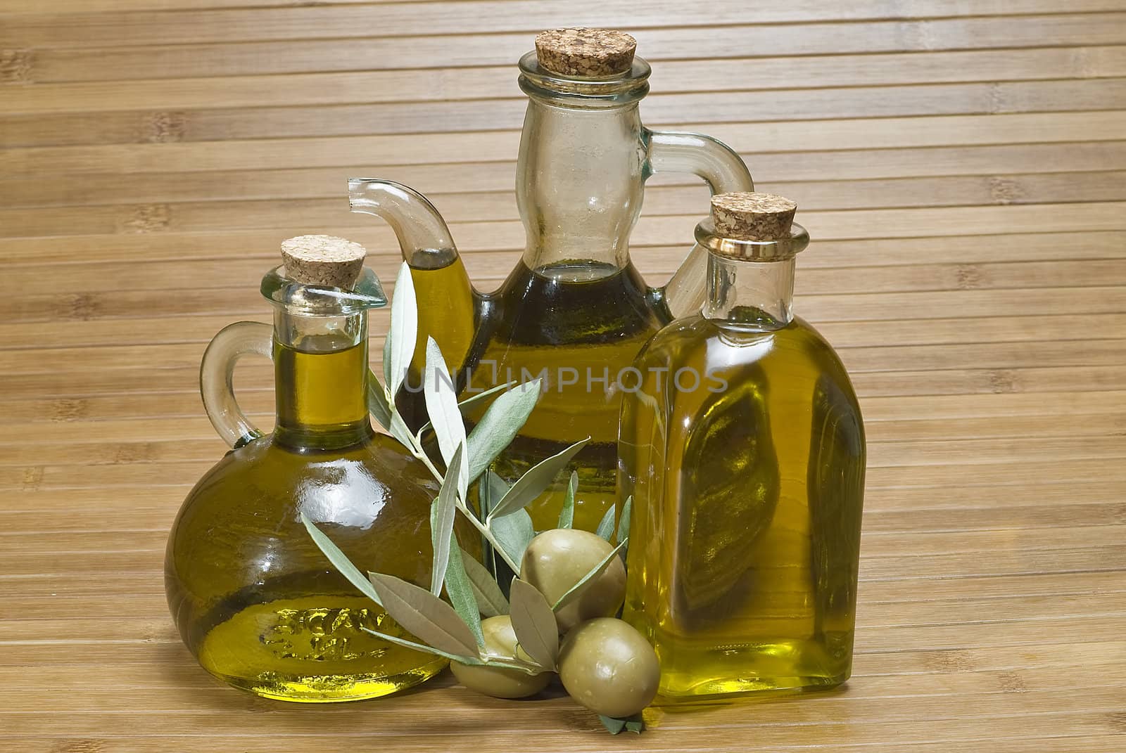 Olive oil bottles and olives on a bamboo mat.