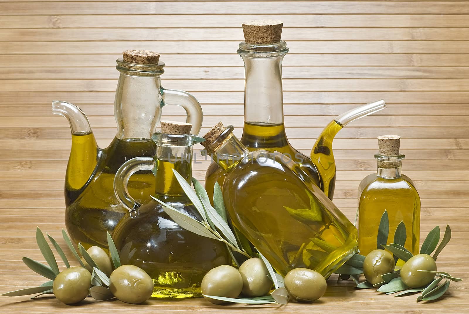 Olive oil bottles and olives on a bamboo mat.