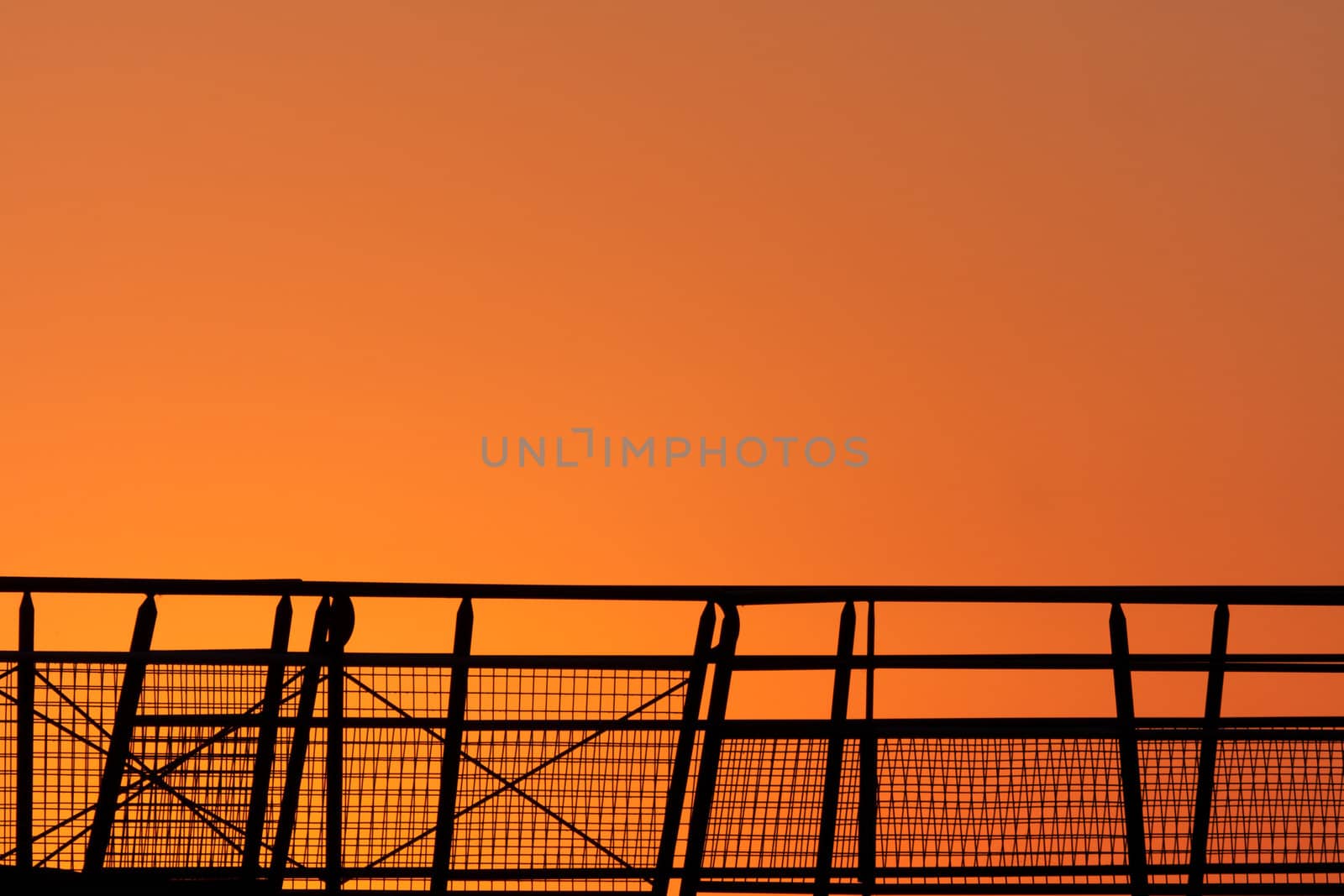 Bright sunrise with a metal railing in the foreground in silhouette