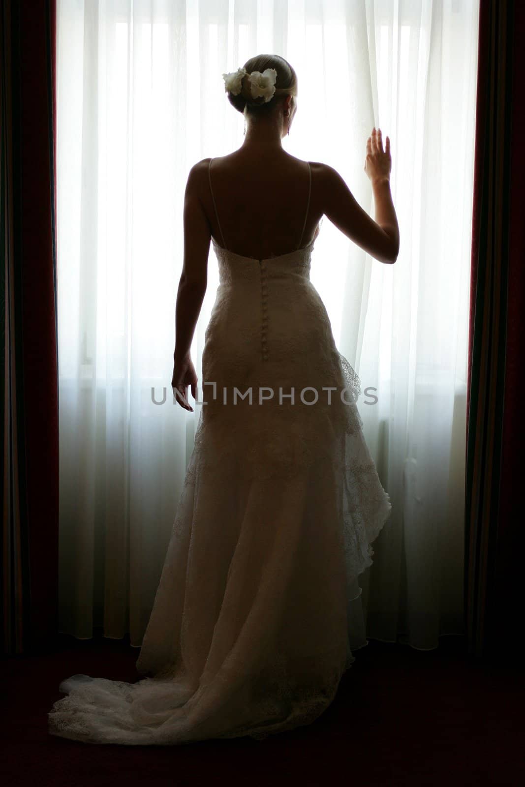 Rear view of young bride in white wedding dress looking out of window.
