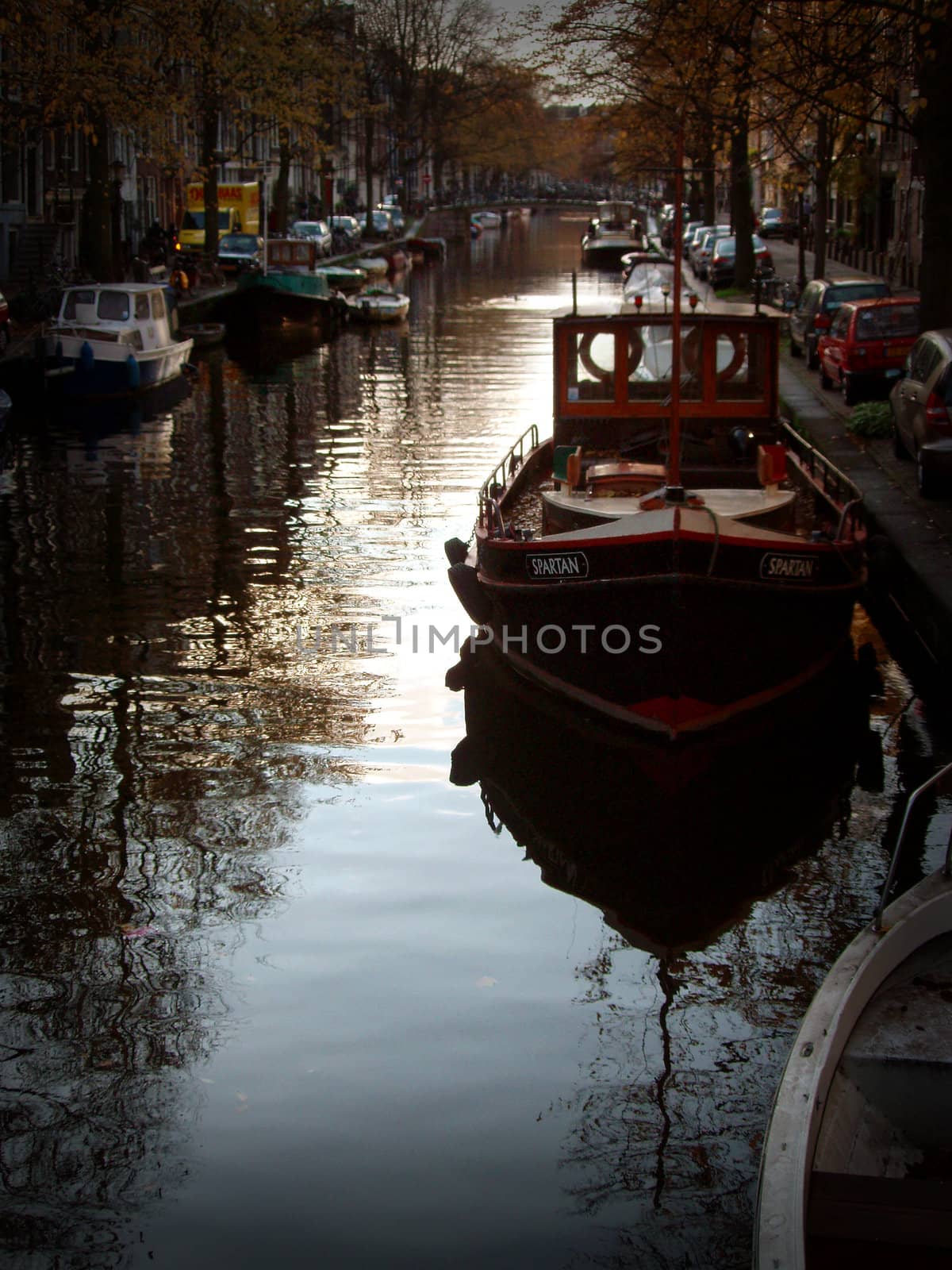 Boat docked on canal in Amsterdam with other docked vessels in the background area of the image.
