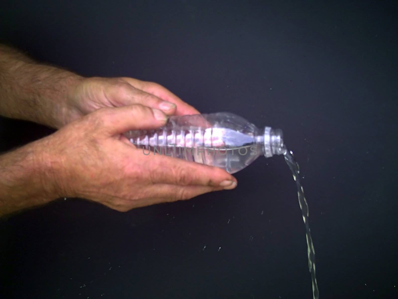 Two hands are holding a bottle and water is pouring out.