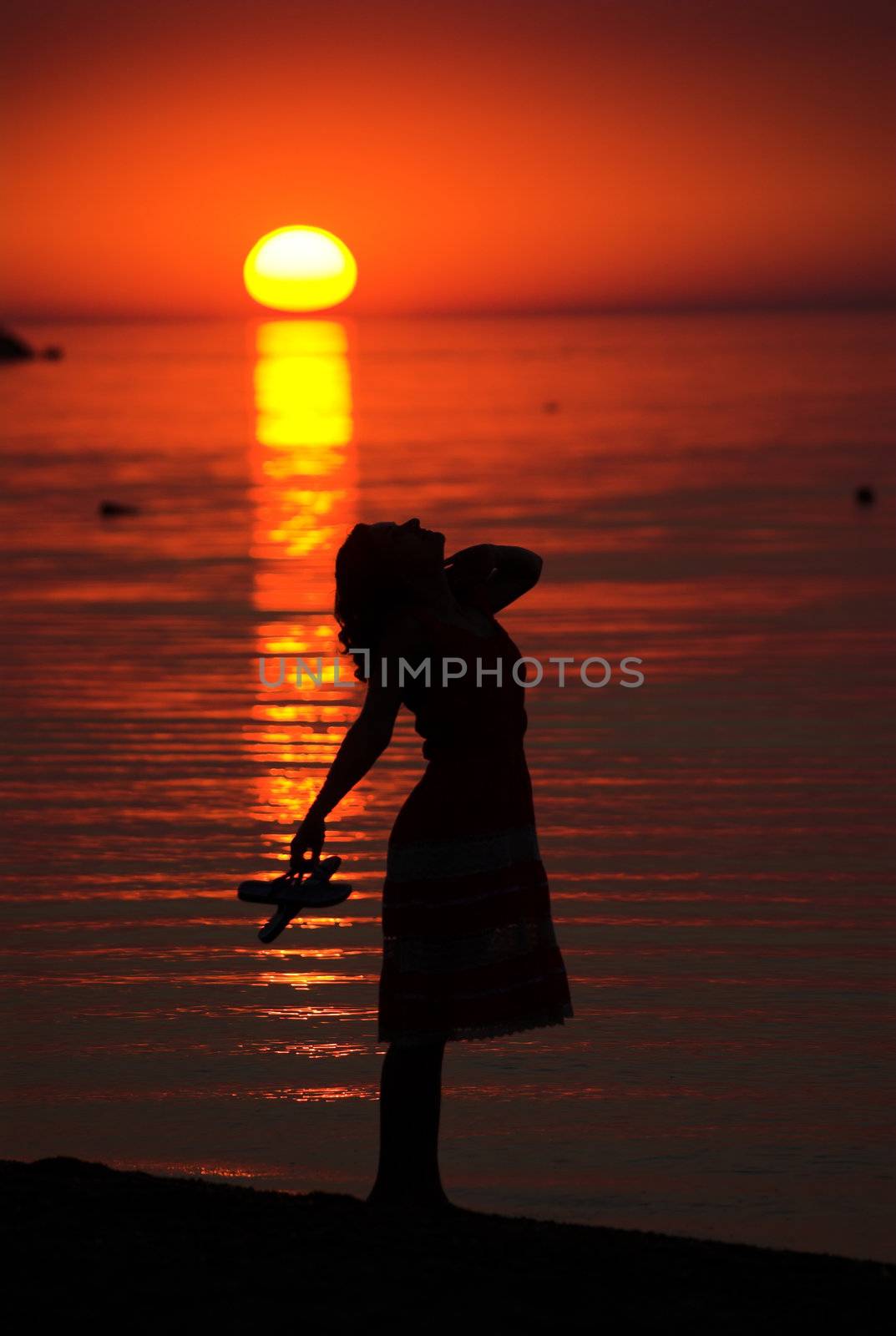 Girl with slippers in her hand is posing on the sea