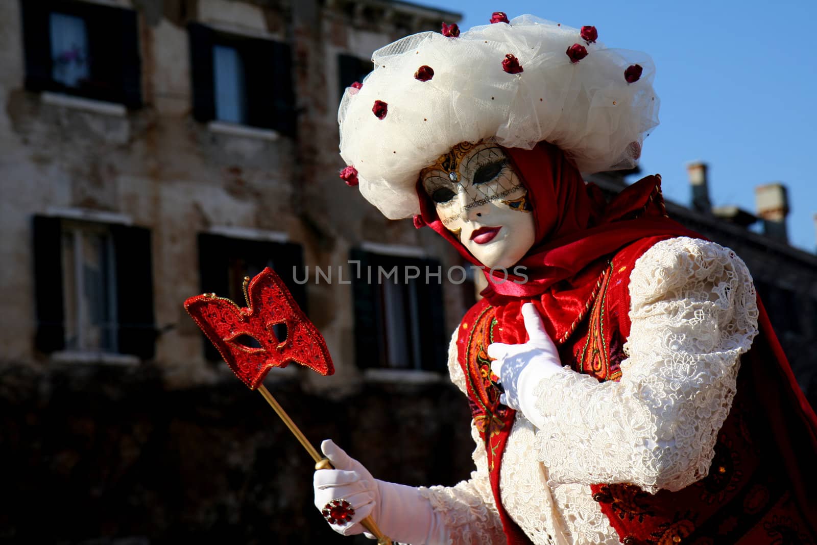 A masked woman with a red eye mask, dressed in white and red, at the Venice Carnival