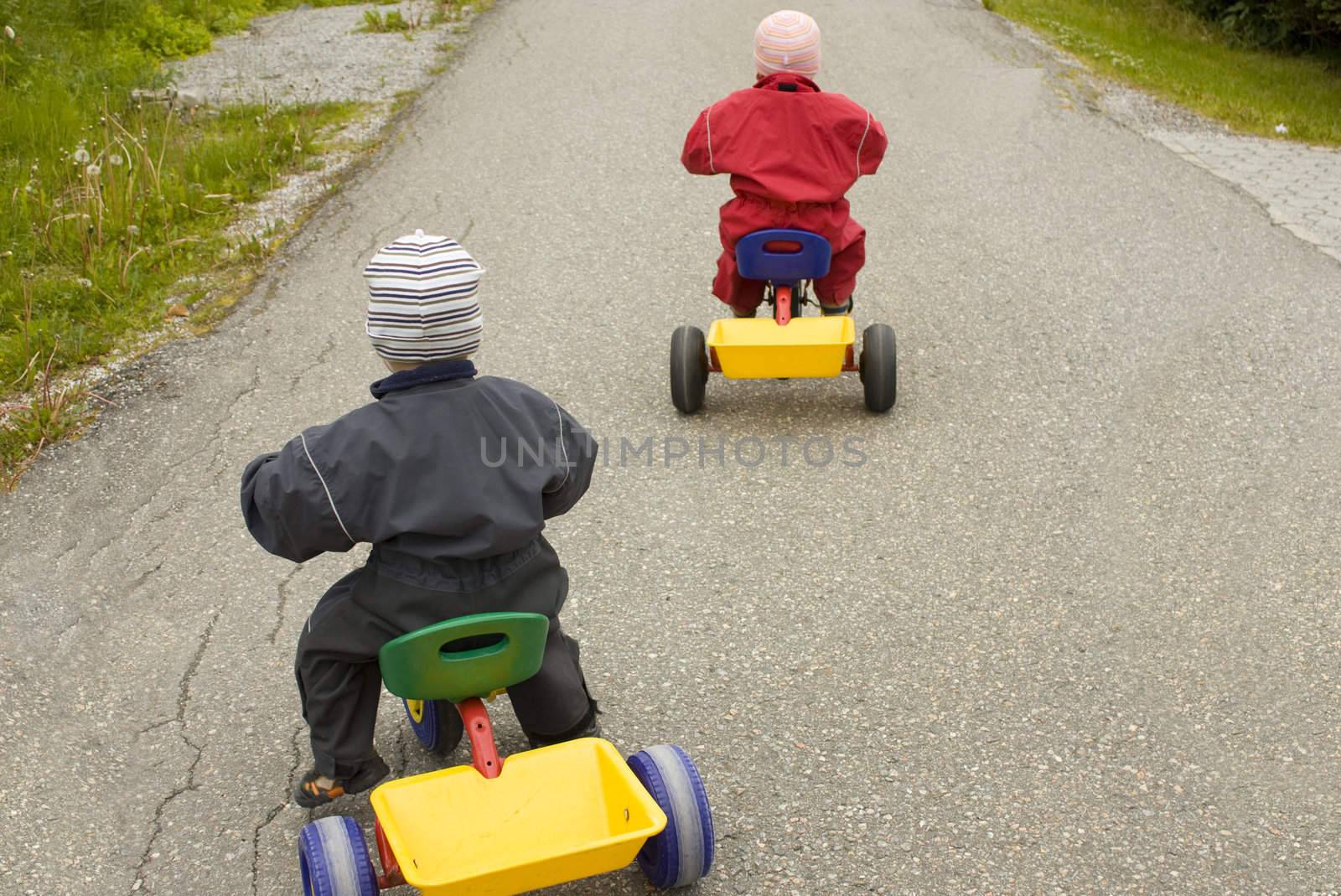 Children racing on tricycles, child in red leading in front of child in blue