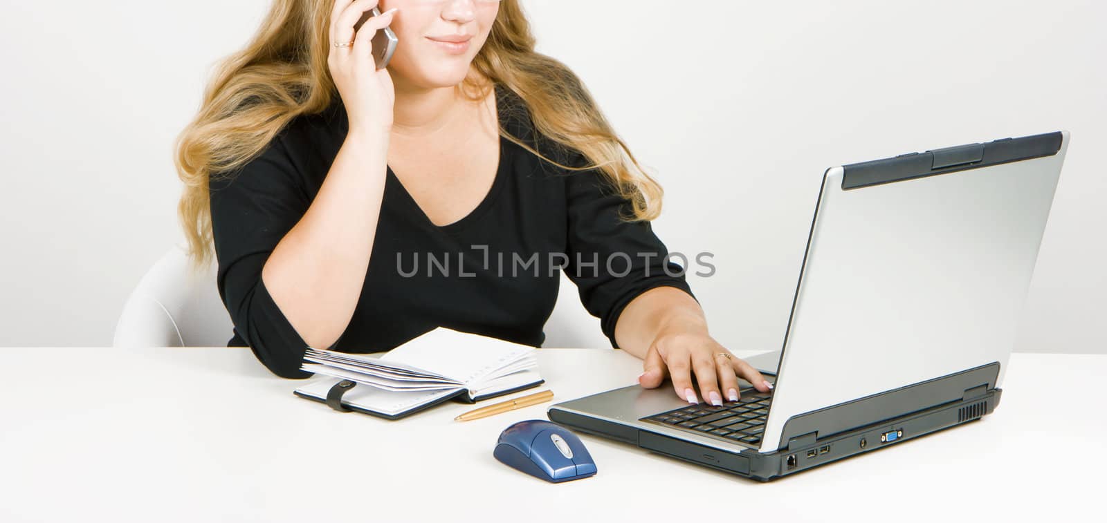 blonde in office with a laptop says on his cell phone
