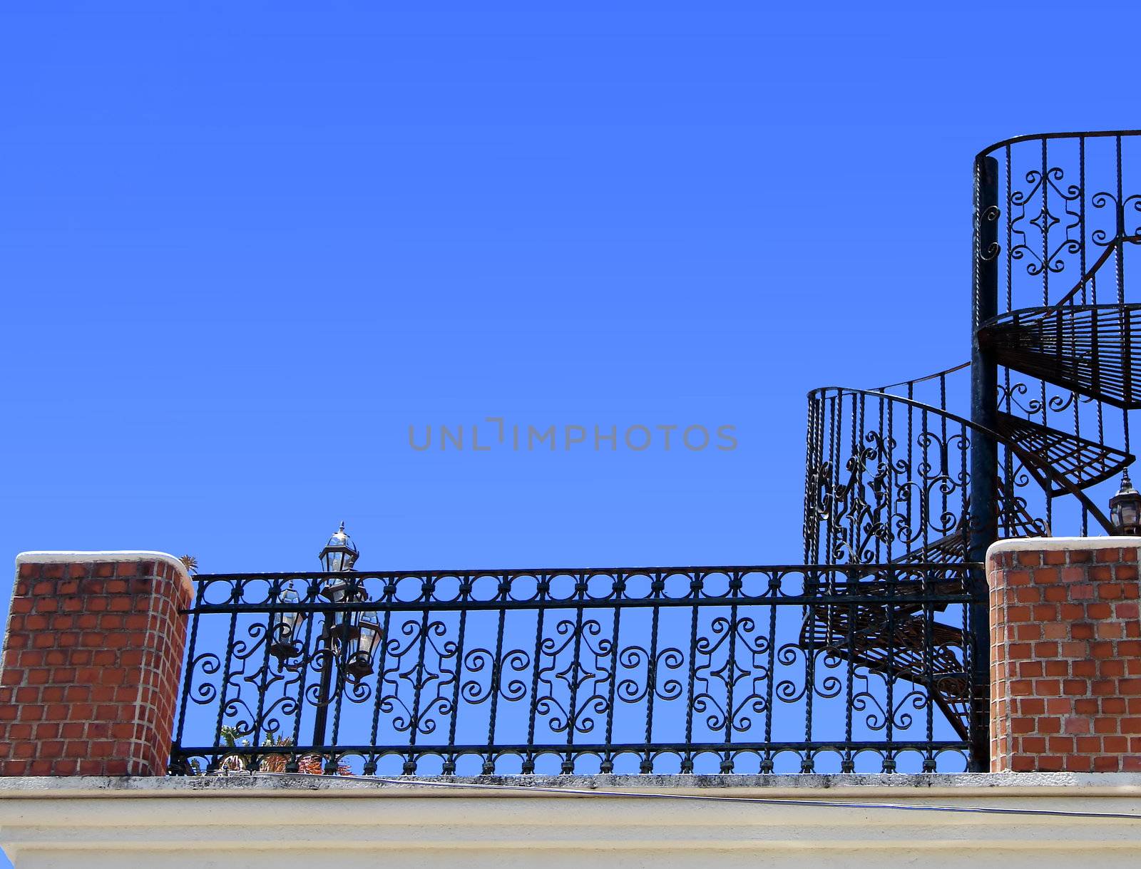 Wrought iron and baliuster outside of old brick building contrasted by bright blue sky