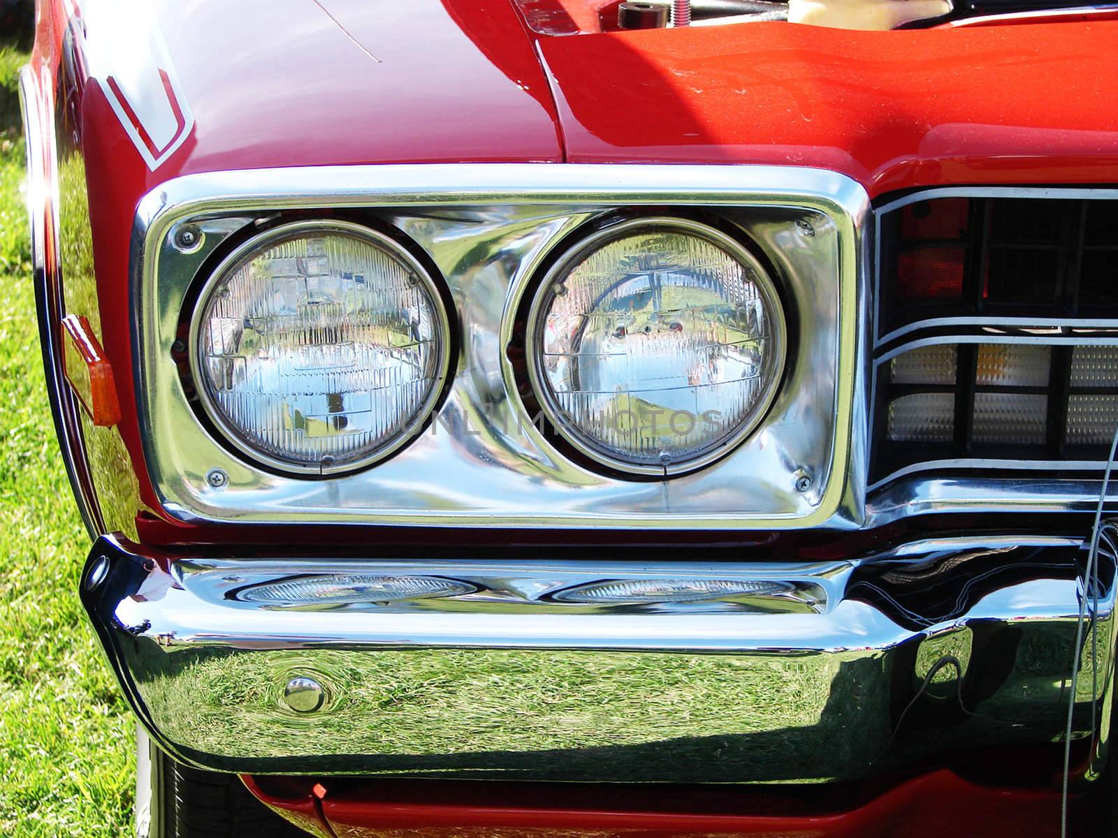 Close-up on the headlights and the chrome bumper of a Hot rod bright red car at a meet show