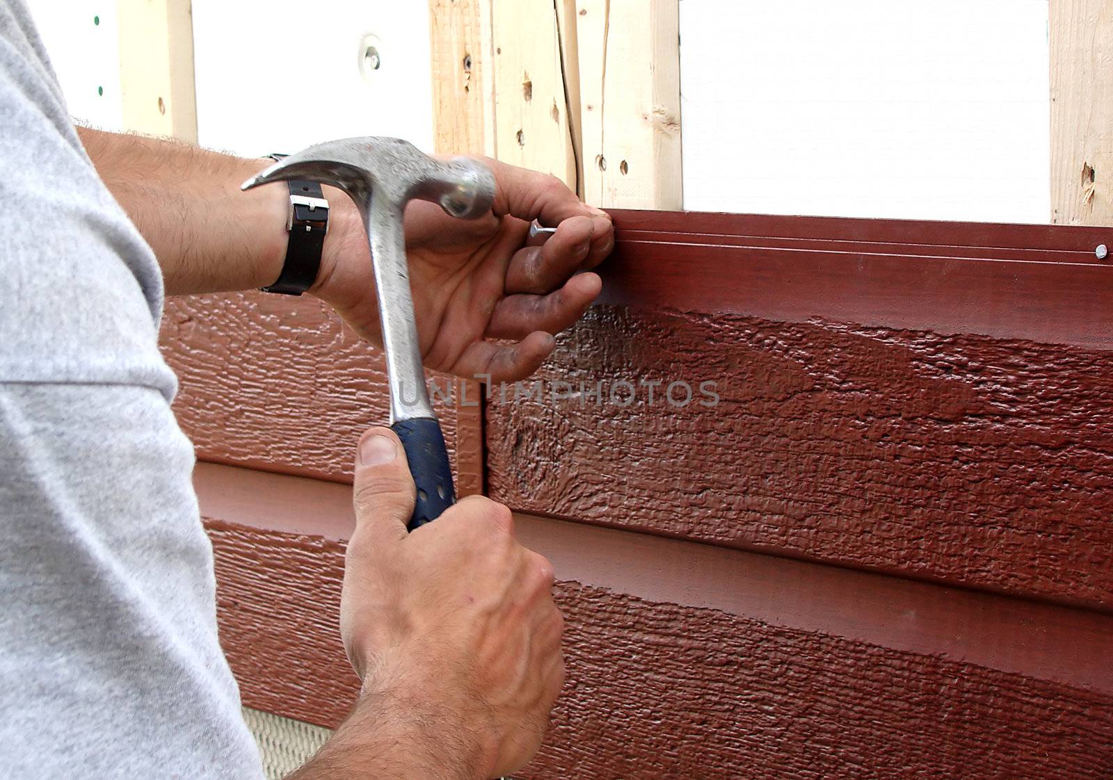 Action shot of a construction worker hammering a nail to put up new siding during major house renovations.