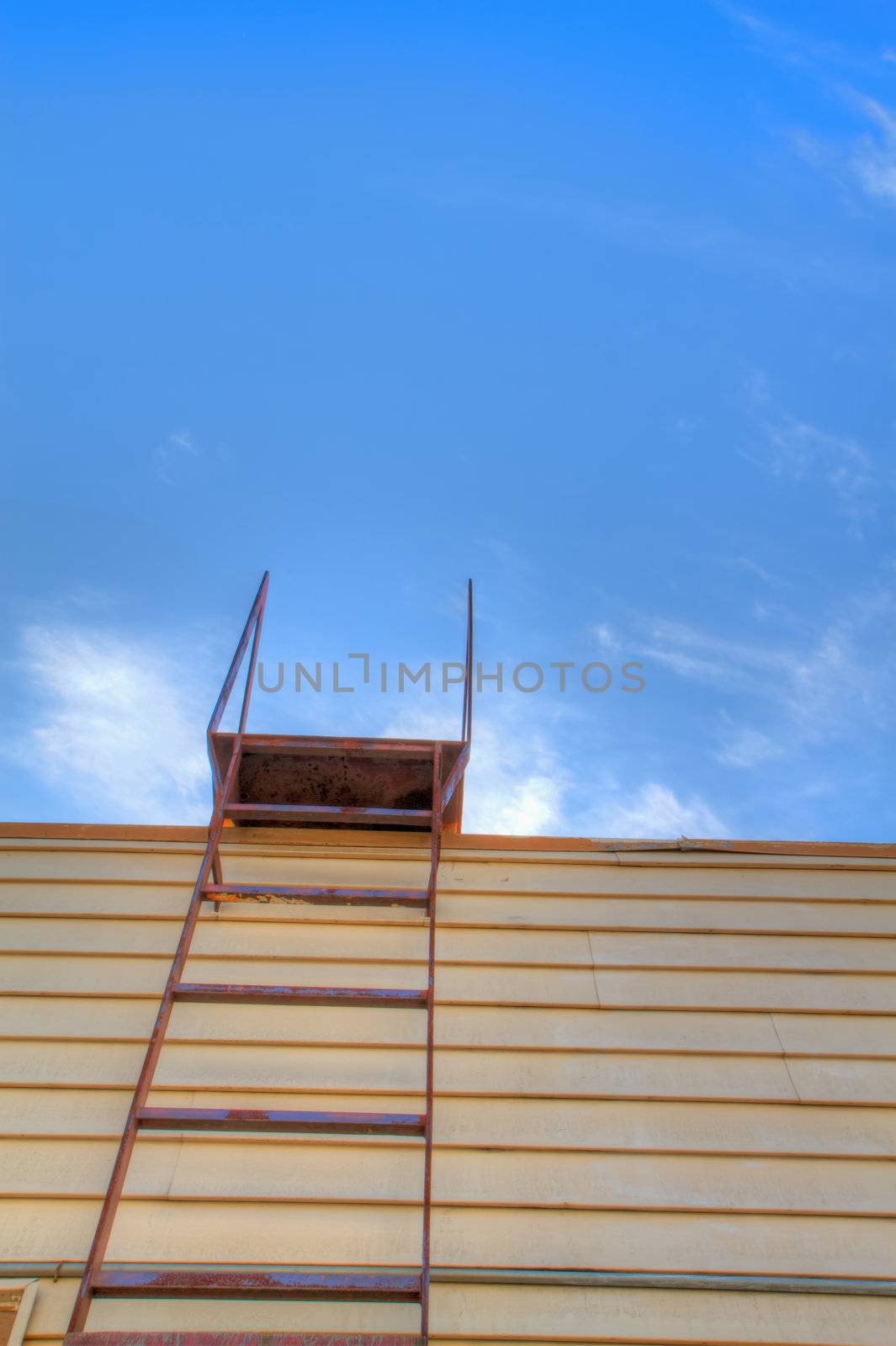 Steel roof ladder on old yellow wood building with white cloudscape blue sky