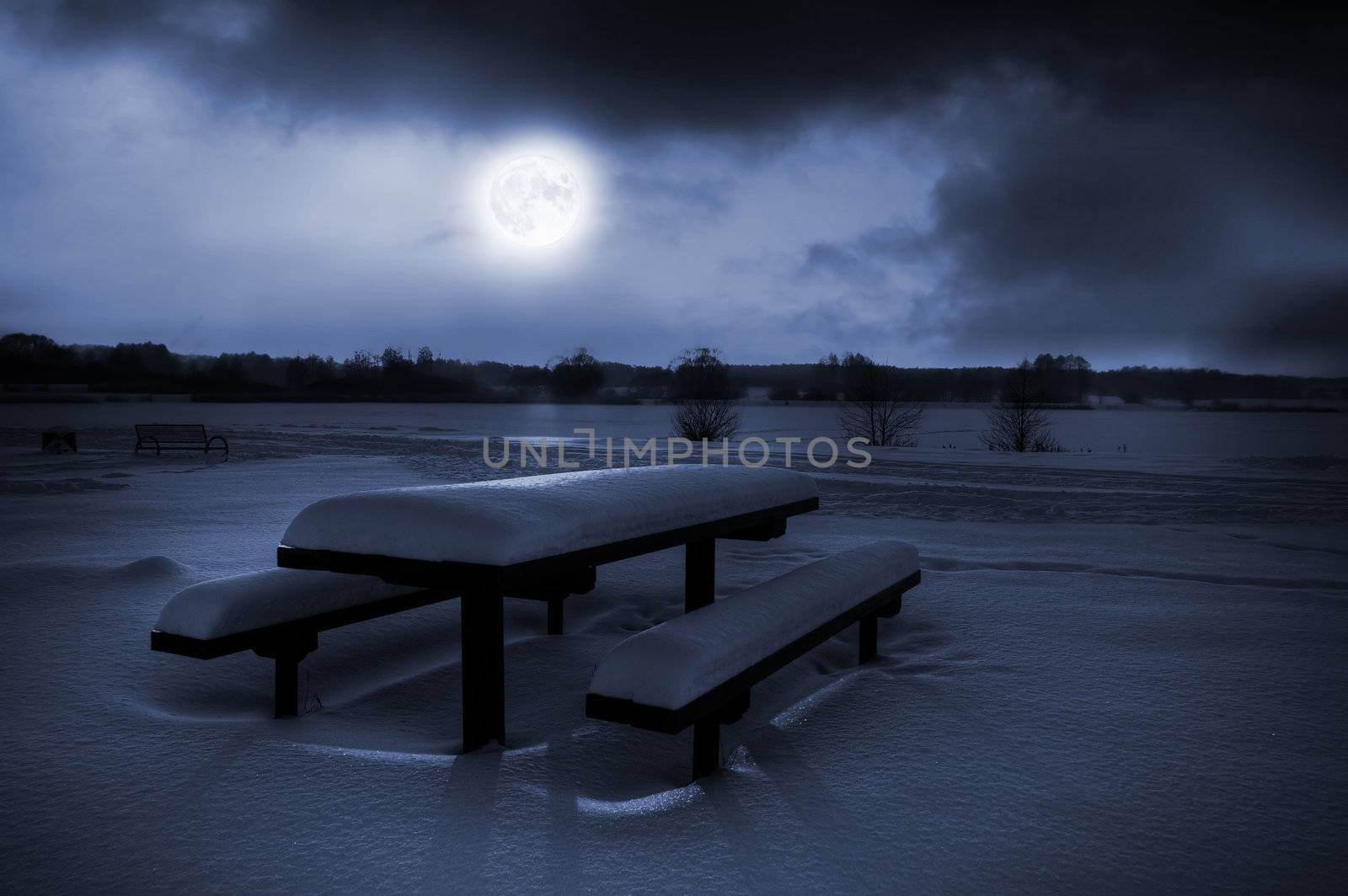 Table and benches covered with snow in moonlight