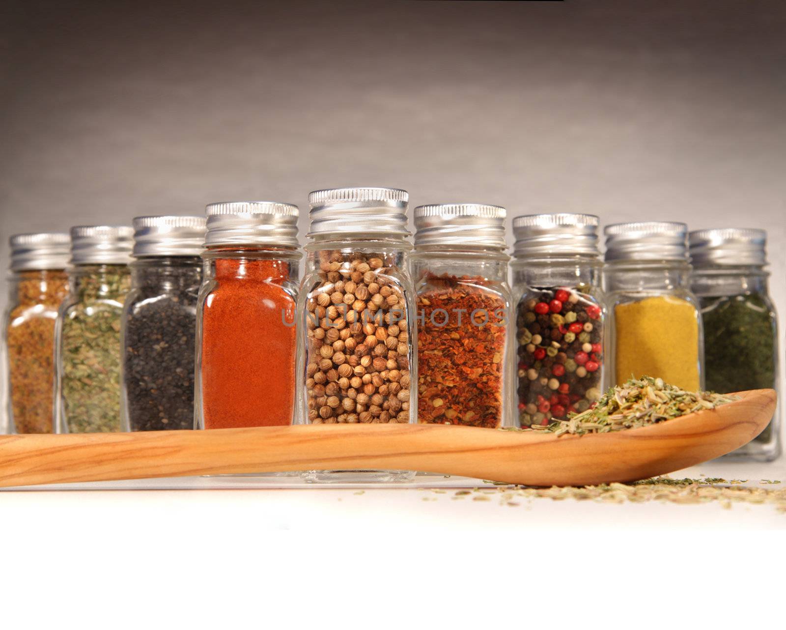 Colorful spices in bottles with wooden spoon