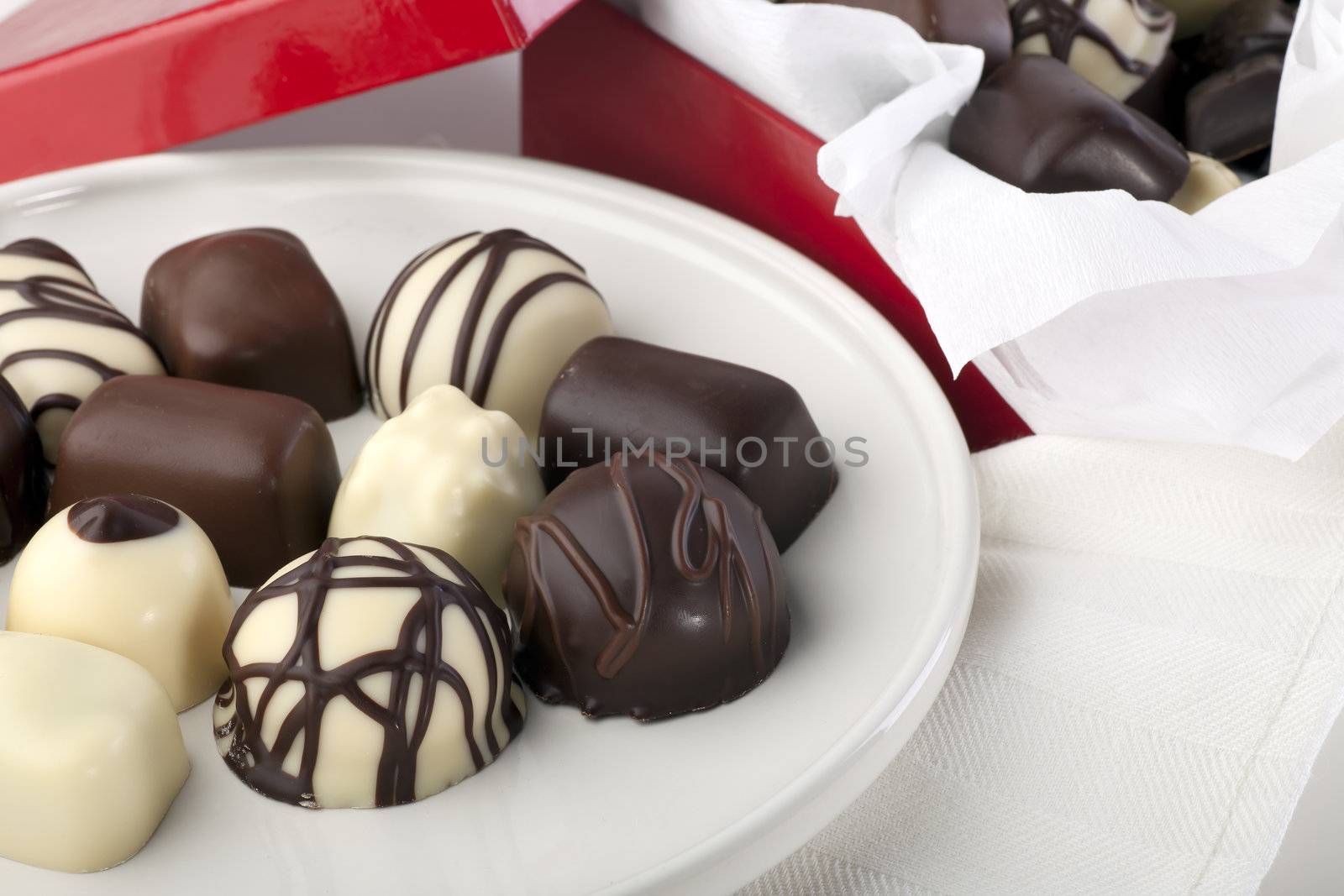 Assortment of gourmet Belgium chocolates on white plate with red gift box.