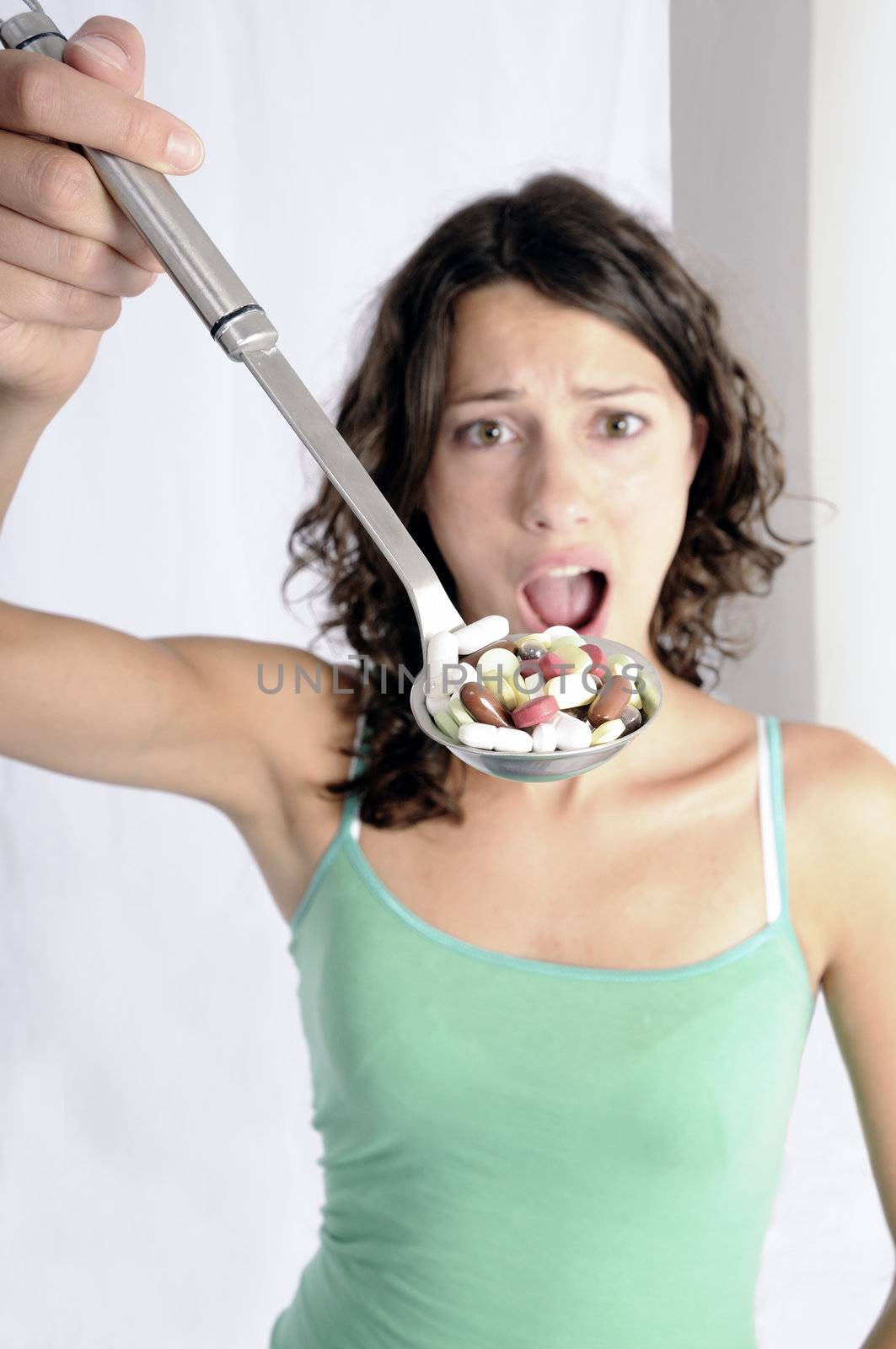 Pretty young woman holding spoon with pile of pills looking skeptical. Concept shot for drug abuse or pharmaceutical industries.