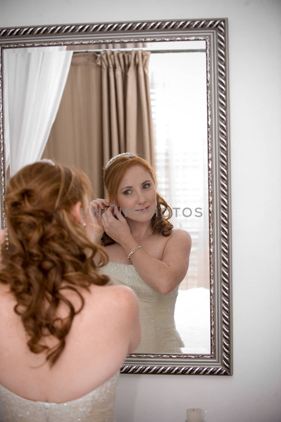 sexy beautiful bride inserting her earrings in whilst smiling by Ansunette