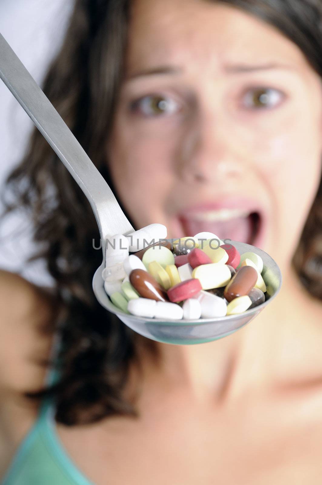 Pretty young woman holding spoon with pile of pills looking skeptical. Concept shot for drug abuse or pharmaceutical industries.