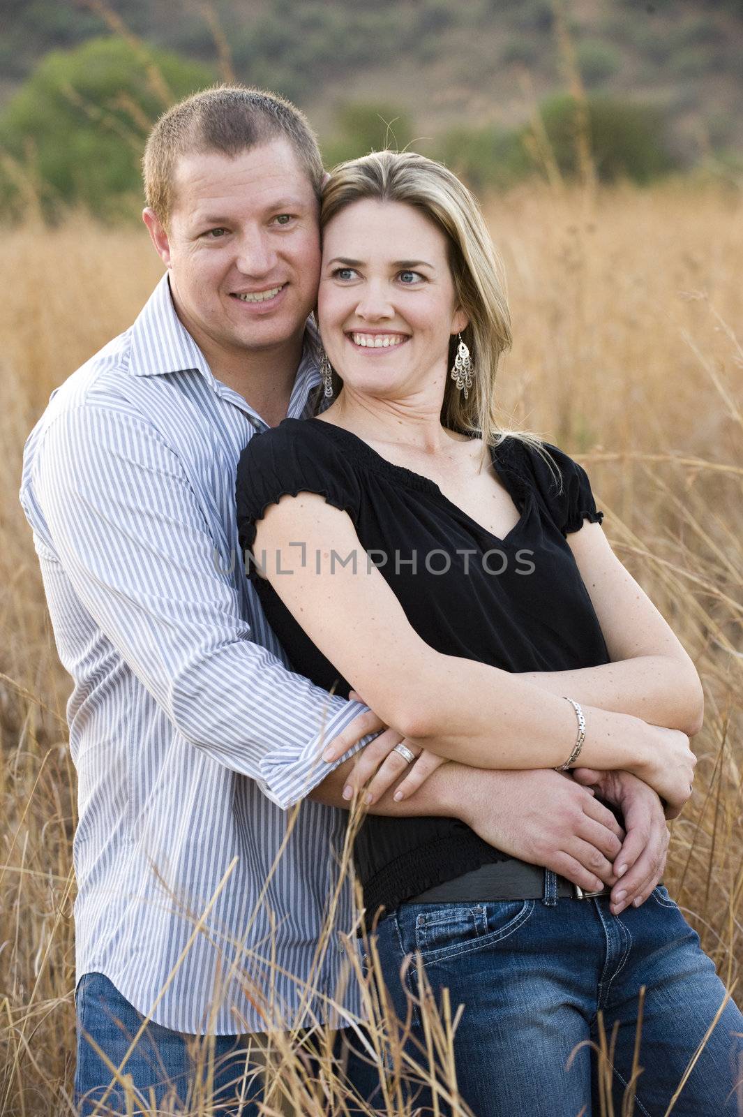 young sexy beautiful blond couple hugging and smiling in long grass at daytime in summer