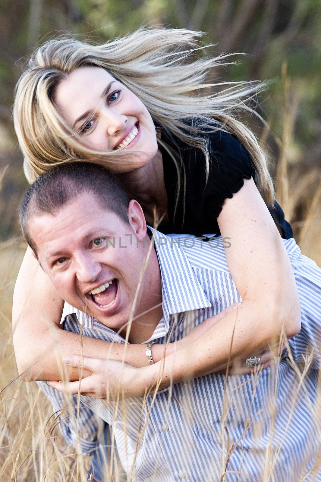young sexy beautiful blond couple carrying and laughing in long grass at daytime in summer