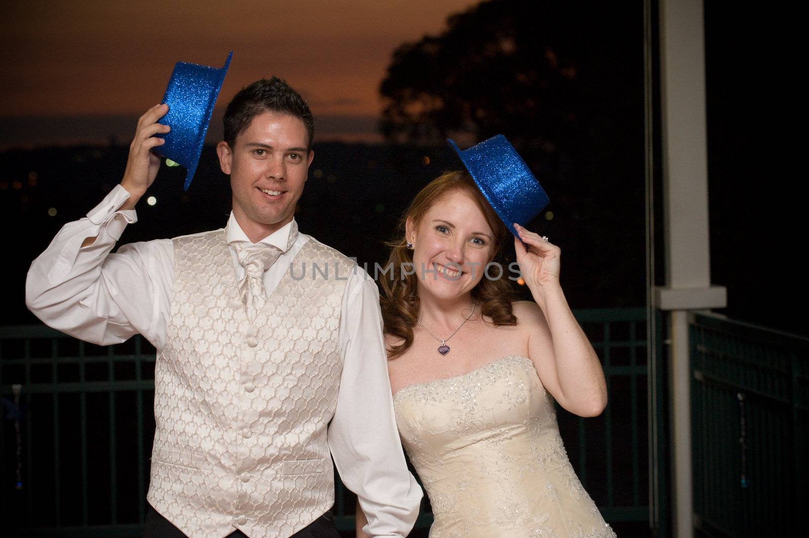 sexy red head bride and her young handsome groom standing with blue hat at sunset outside whilst smiling