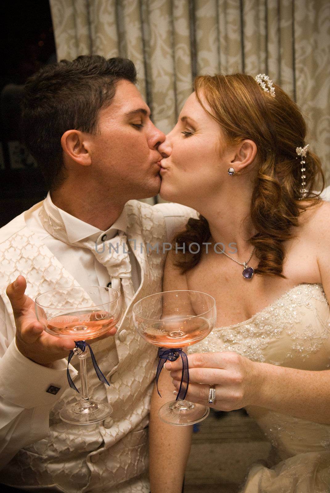 sexy beautiful young bridal couple kissing and holding champagne glasses by Ansunette