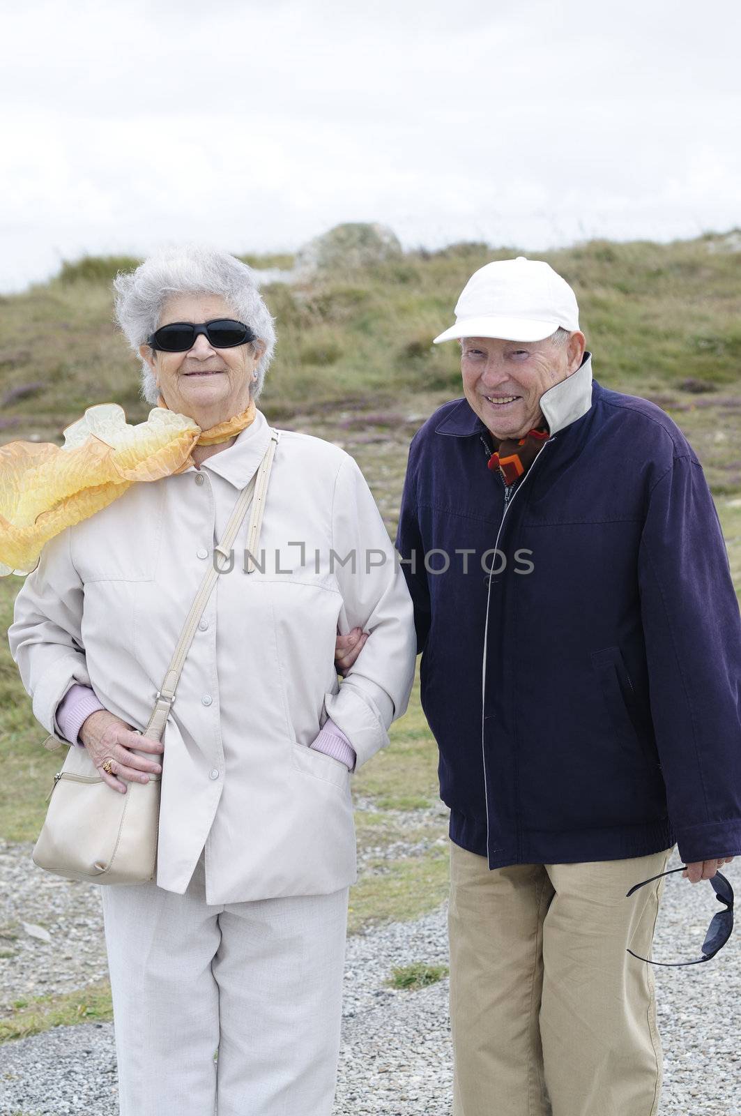 Old senior couple walking along the coast holding their hands and smiling.