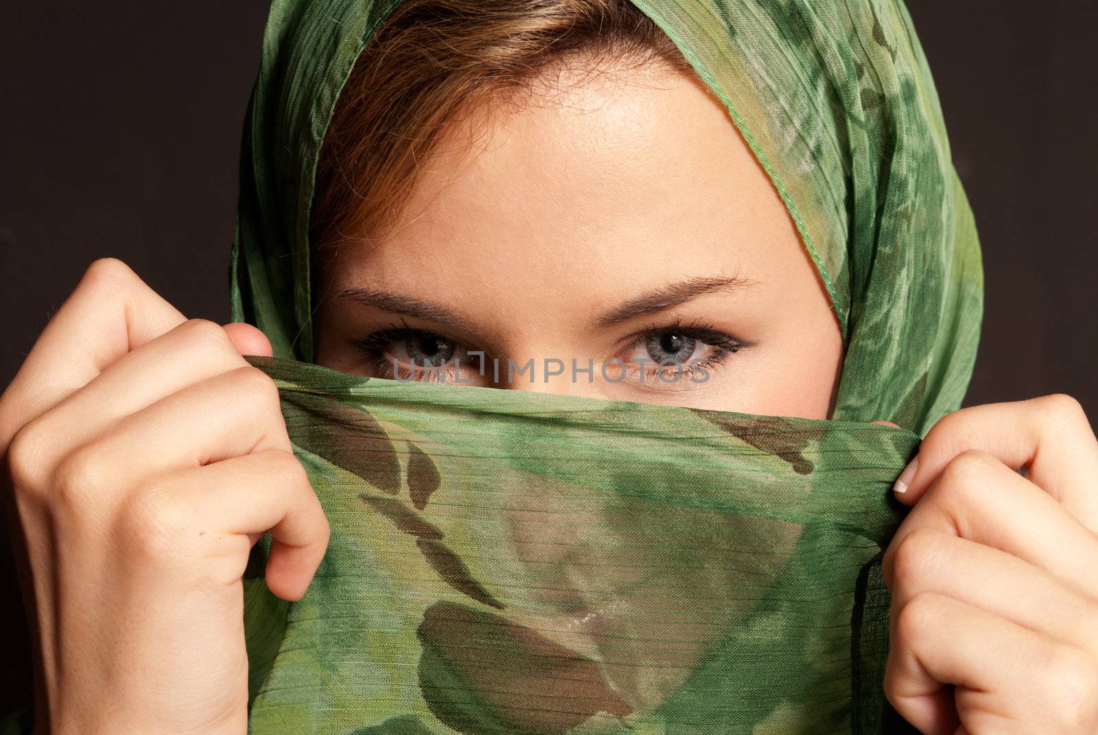 Young arab woman with veil showing her eyes on dark gray background