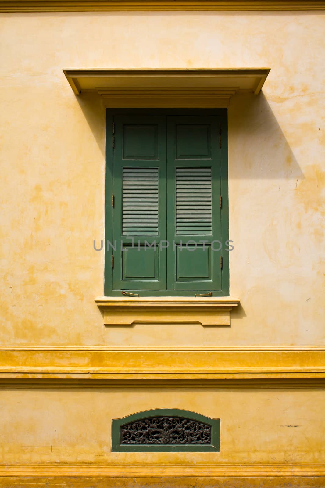 green window shutters on yellow wall with great shadows