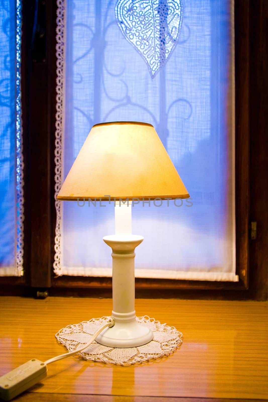 Old lamp on wooden window shelf with dusk in the background.