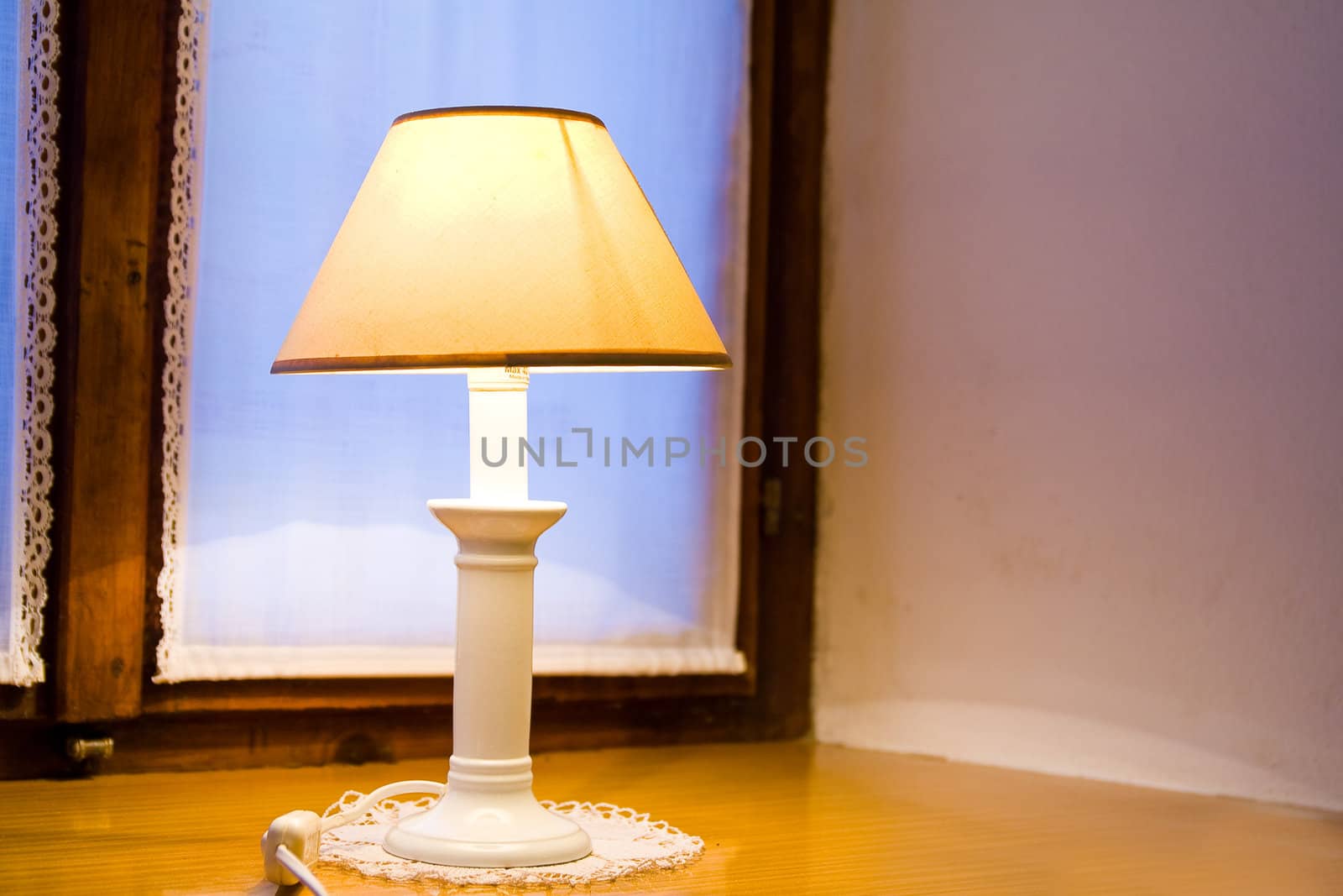 Old lamp on wooden window shelf with dusk in the background.