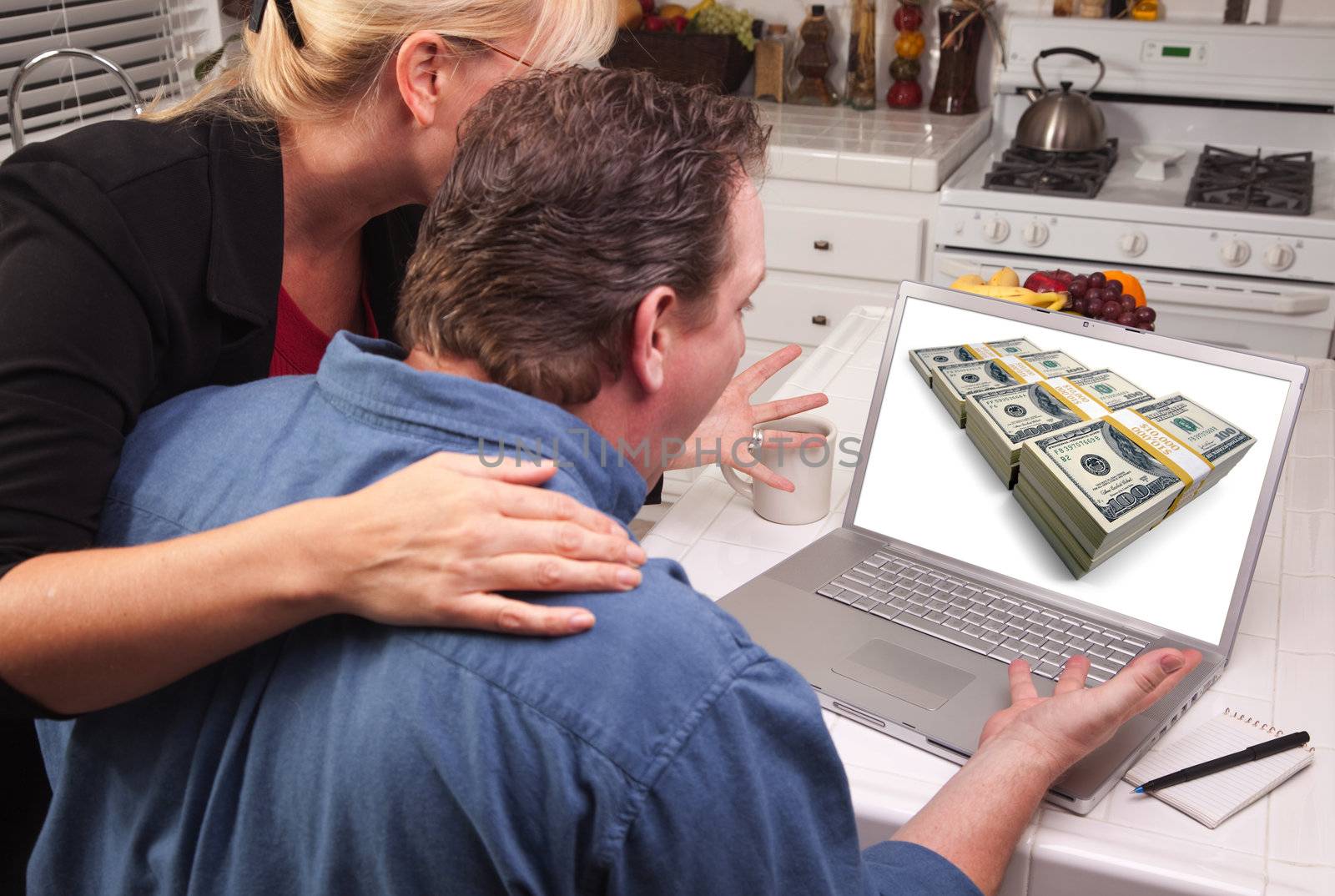 Couple In Kitchen Using Laptop with Stacks of Money on the Screen.