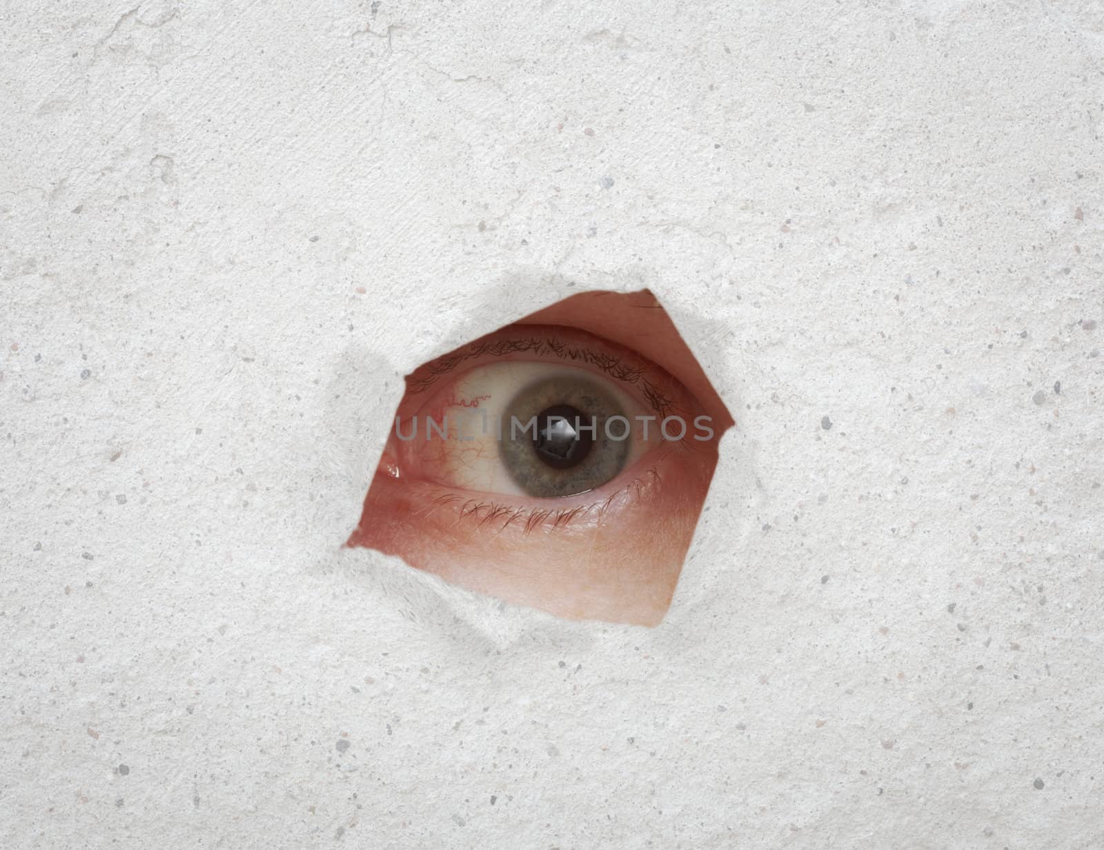 Eye looking through a hole in the rough gray wall