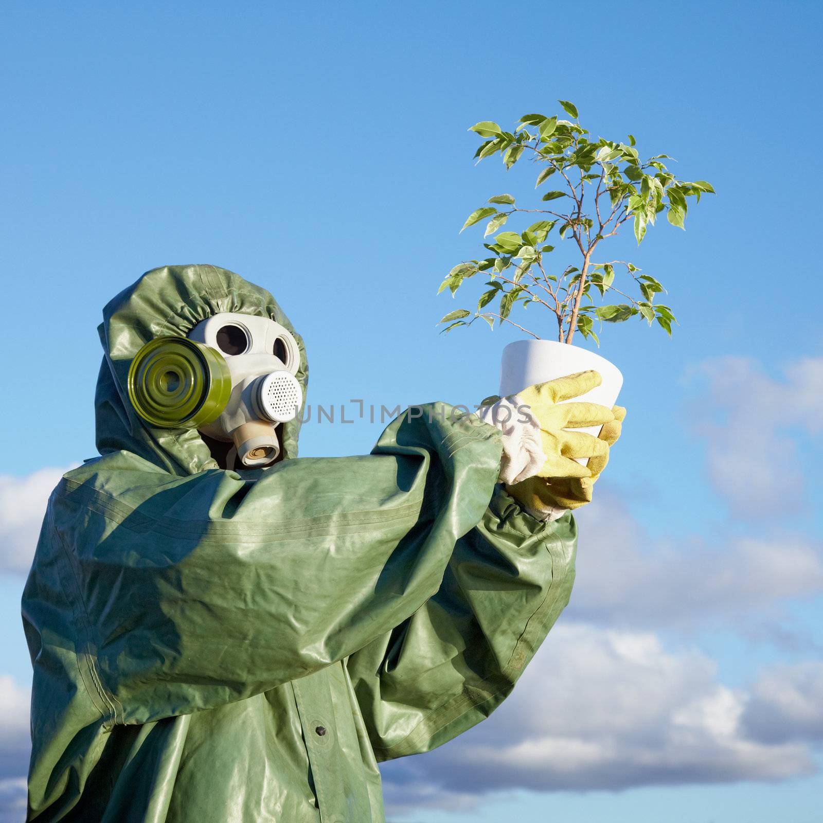 A man in a chemical suit and gas mask with a plant in the hands