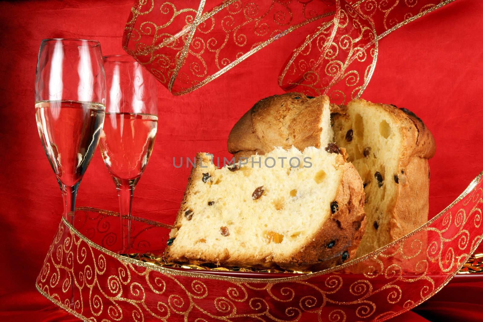 Panettone the italian Christmas fruit cake served on a red glass plate over a red background with golden star decorations, ribbon and two glasses of champagne. Selective focus.