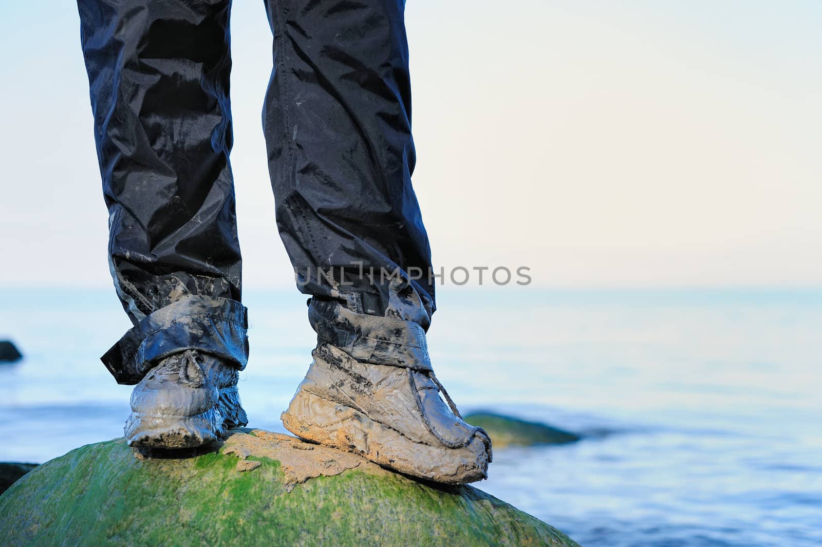 Legs in dirty boots on the moss-grown boulder on the shore