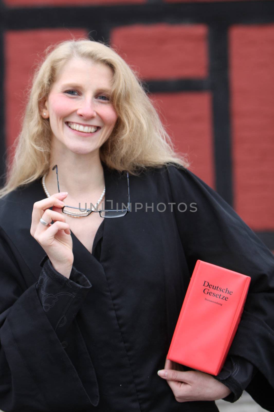 Friendly smiling law student or lawyer with red law book under his arm and glasses in hand
