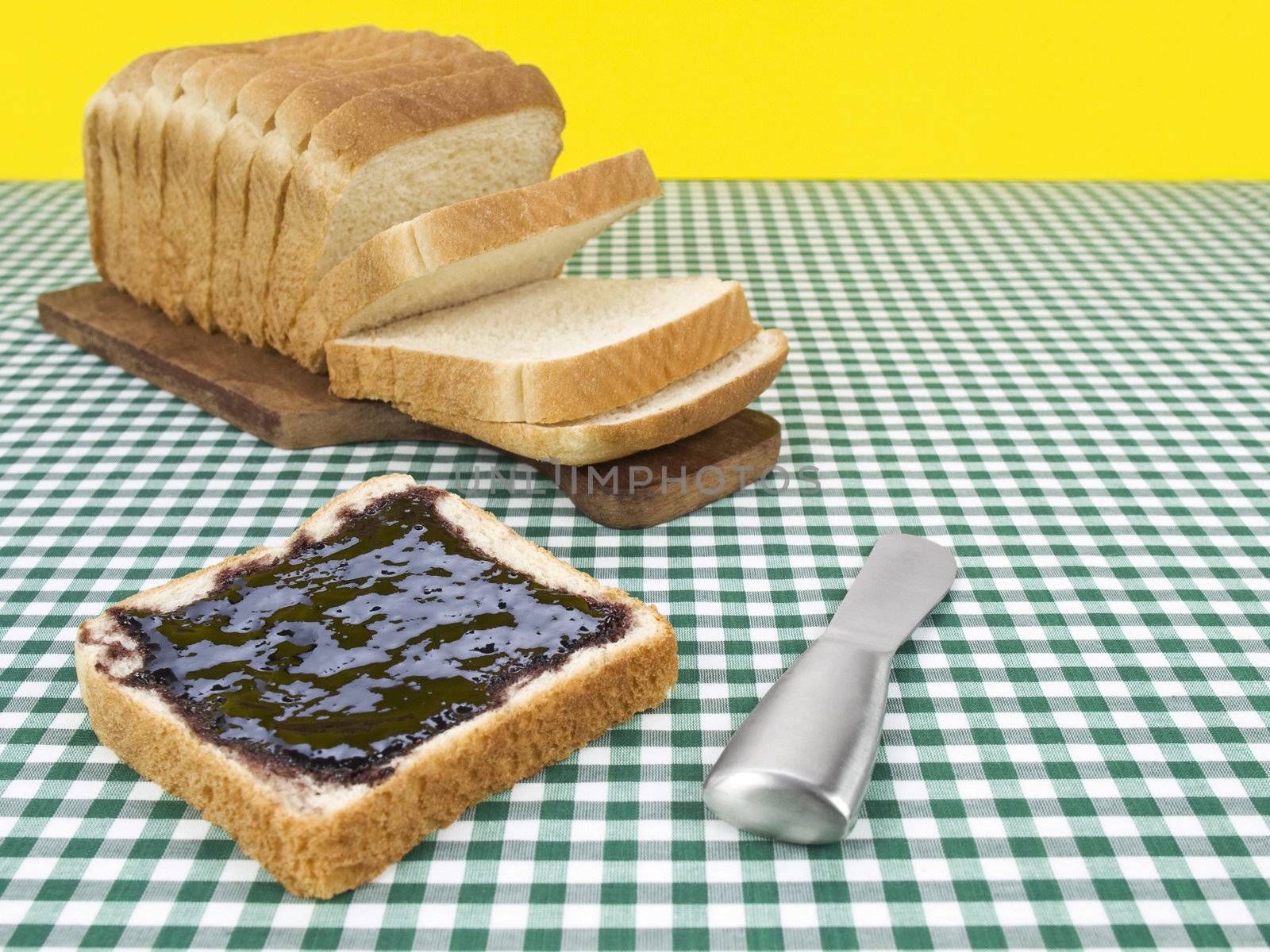 A slice of bread spread with jam beside the loaf of bread.