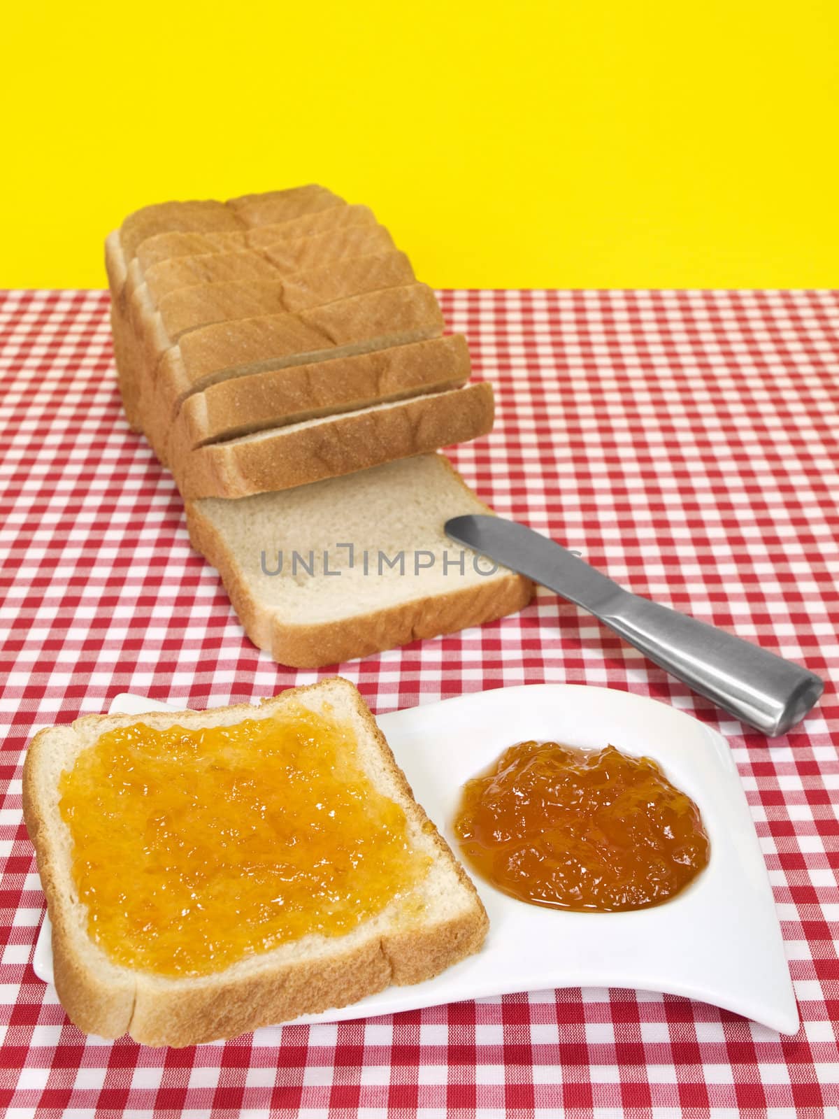 A slice of bread spread with jam beside a loaf of sliced bread.