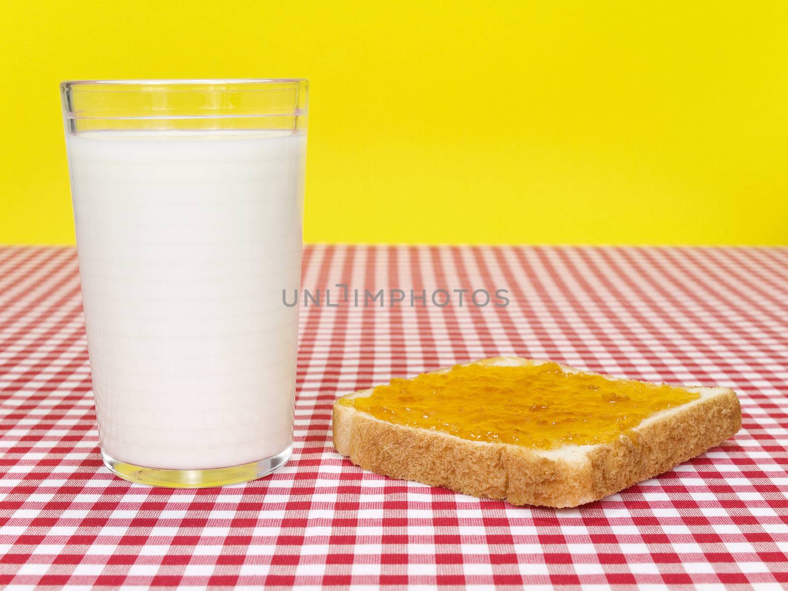 A glass of milk and a toast spread with jam over the table.