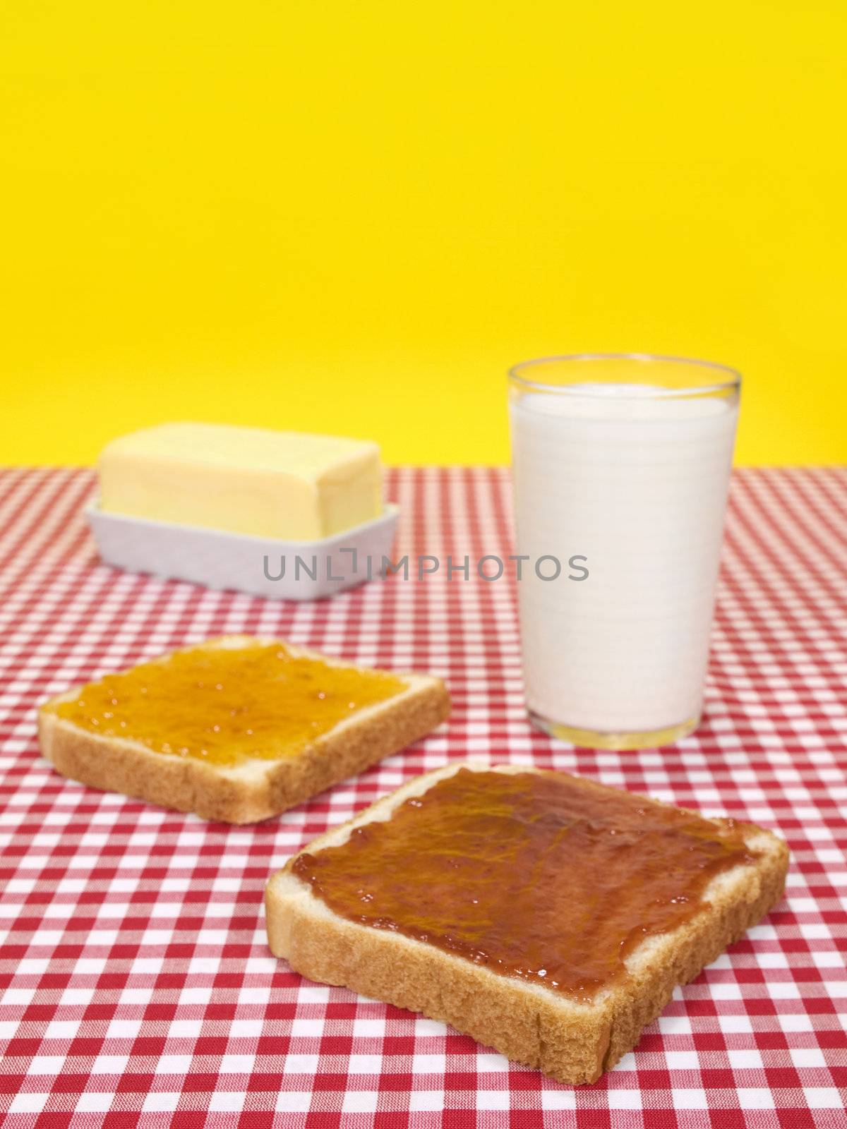 Two slices of bread spread with jam, a glass of milk and a butter stick.