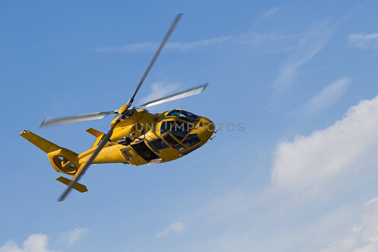 Yellow helicopter flying in blue sky with clouds