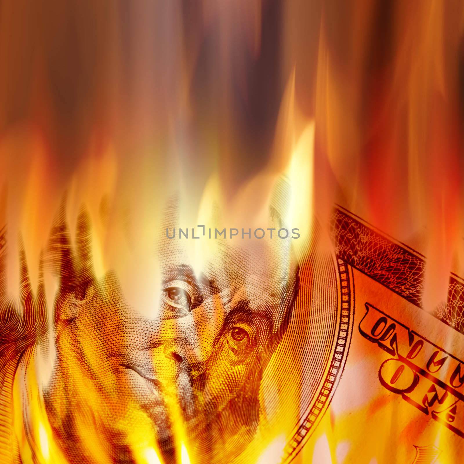 Burning American money with Benjamin Franklins face appearing on fire on a one hundred dollar bill.