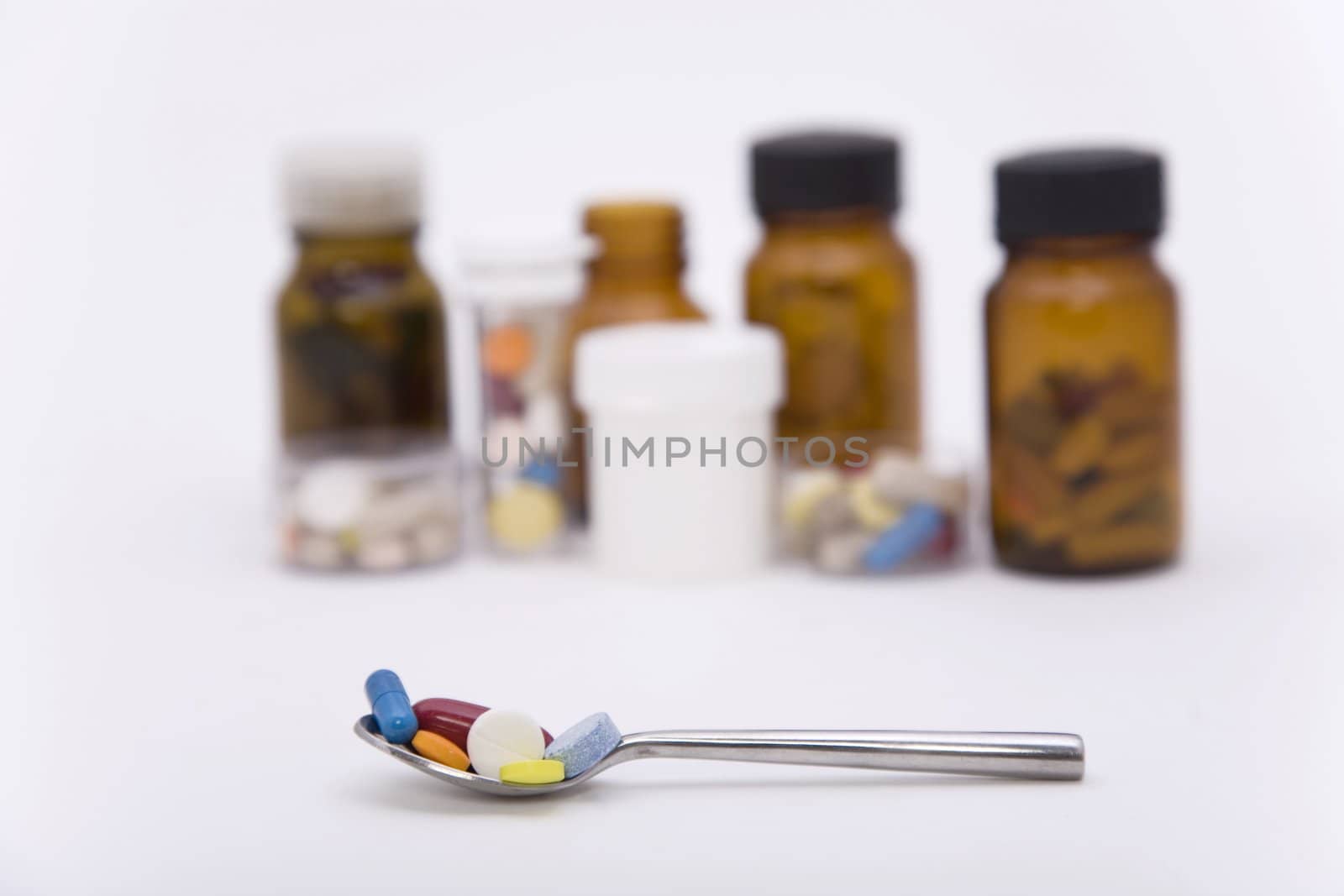 differently colored pills in spoon with other pills on the background