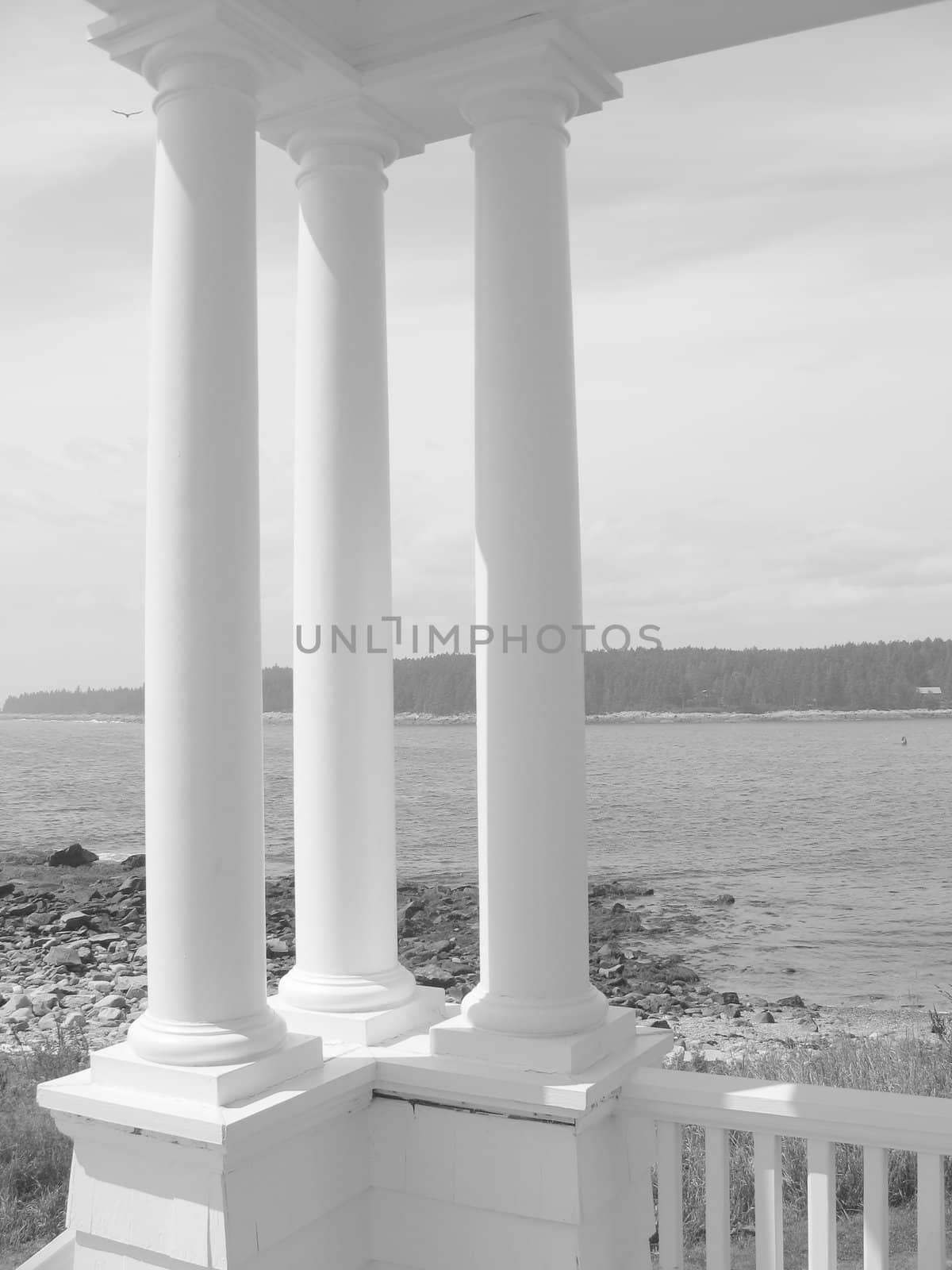 Three 19th century architectural columns at the ocean's edge, in black and white